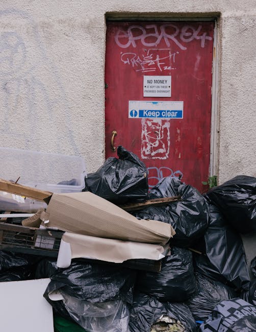 A middle-aged man dressed in a black T-shirt and dark trousers is seen using a wooden-handled litter picker to sort rubbish into a large white plastic bag. He is leaning forward, placing waste into th